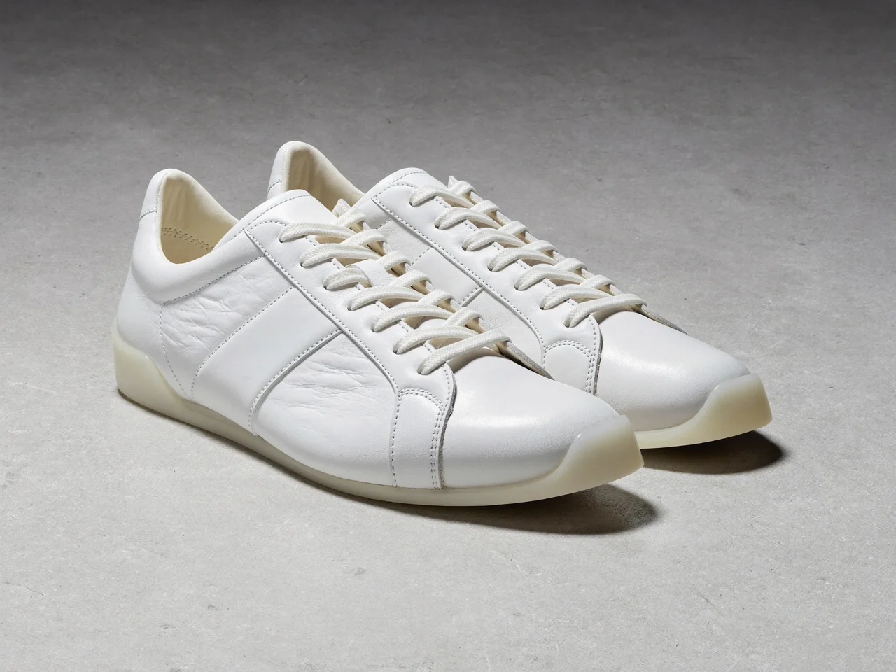Weisse Low-Top-Sneaker aus Leder auf heller Betonfläche, illustriert