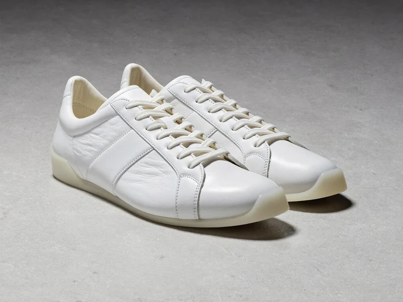Weisse Low-Top-Sneaker aus Leder auf heller Betonfläche, illustriert